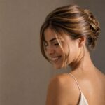 Fotografia editoriale di una ragazza sorridente, femminile con un raccolto elegante e strutturato, su sfondo neutro scuro. Luce radente che valorizza
